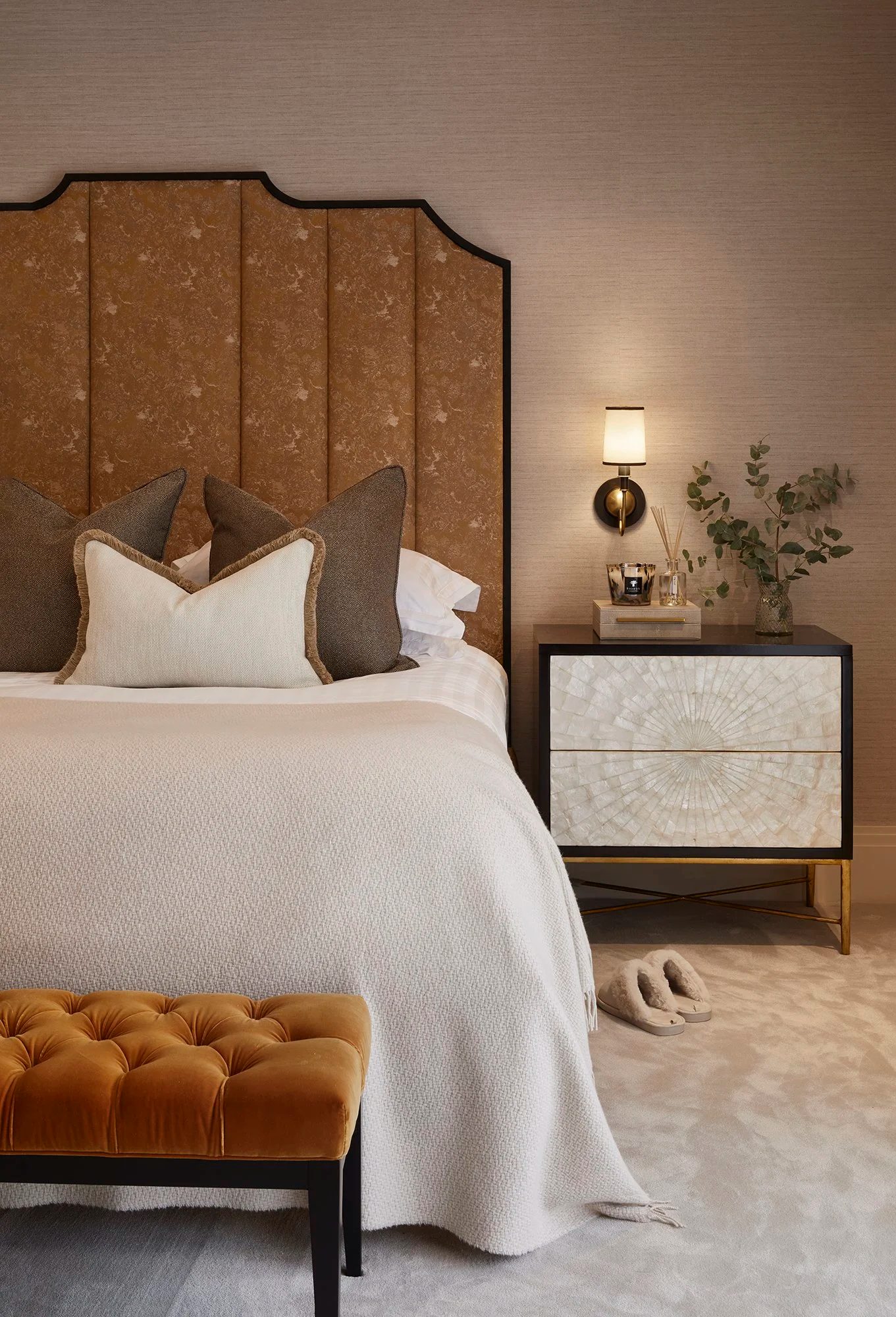 Bedroom with ochre upholstered headboard and mother-of-pearl bedside chest