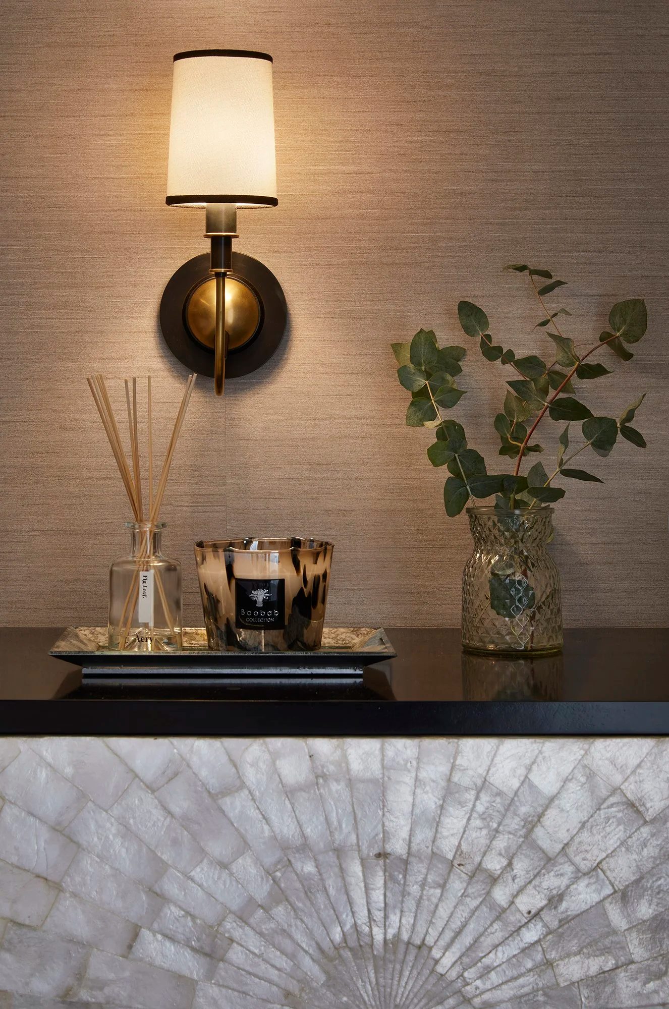 Brass wall light, scented candle and eucalyptus on a grasscloth wall